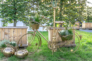 Ein zauberhaftes, ganz in Gold getauchtes Fahrrad steht als strahlendes Symbol der ewigen Liebe auf sattgrünem Rasen. Jeder Korb ist ein kleines Nest aus frischem Grün, zarten weißen Blüten und liebev