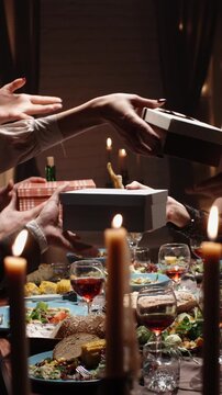 Vertical cinematic slow motion video hands giving and receiving gift boxes over festive table warm light cozy atmosphere concept christmas holiday lifestyle friendship gratitude joy