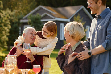 Senior Caucasian woman sitting outdoors being hugged by young girl while middle aged woman and man...