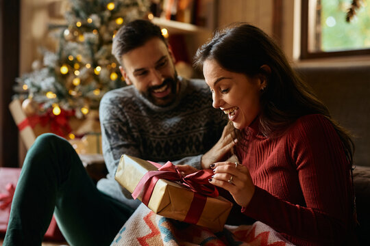 Happy woman receiving Christmas present from her boyfriend at home. - Powered by Adobe
