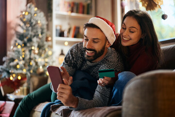 Happy couple using smart phone and credit card while buying online on Christmas.