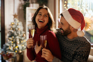 Joyful couple drinking champagne while celebrating Christmas at home.