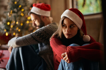 Young displeased woman sitting back to back with her boyfriend after having argument on Christmas day at home.