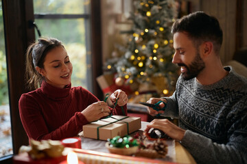 Young smiling couple wrapping Christmas presents at home.