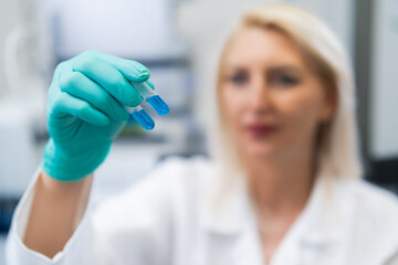Blonde woman scientist studung blue biochemical solution in test tube
