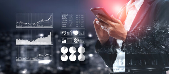 A business professional stands in a modern urban environment, using a smartphone while analyzing...