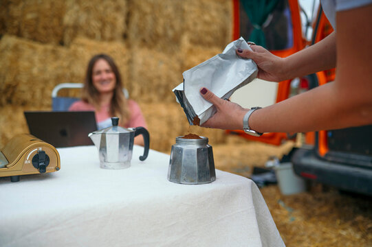 Woman pouring ground coffee into moka pot at table.
