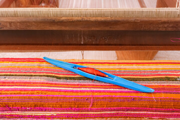 Colorful handwoven silk fabric on traditional loom with blue shuttle and red thread, handmade textile craft background showing weaving process and vibrant yarn pattern for cultural design concept.