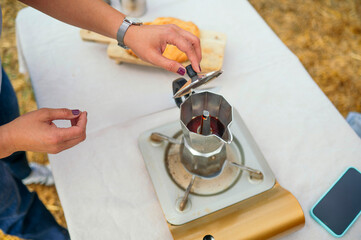 Woman checking moka pot while brewing coffee outdoors.
