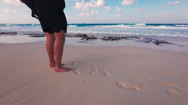 Close-up view of person standing barefoot at shoreline, with gentle waves washing over smooth sand. Tranquil coastal scene evoking summer leisure and freedom. Marsa Matrouh governorate, Egypt