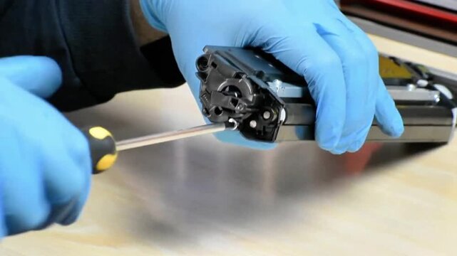 Disassembling a laser printer toner cartridge using a screwdriver. Step-by-step screw removal and casing separation reveal internal components and structure