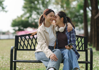 Young asian women sharing happy moment sitting on park bench