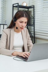 Asian businesswoman adult female operator headset on, typing during remote meeting, communicating with client online, providing consultation and support in corporate professional customer service