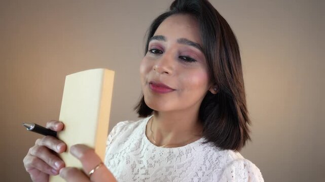 Head-shot close up of happy positive motivated young woman holding book and pen looking at camera smiling feels happiness positivity joy, isolated over grey background.