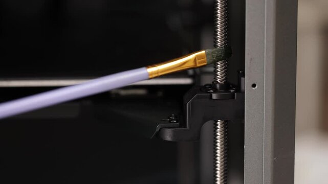 Applying lubricant with a brush on the threaded rod inside a 3D printer, concept of maintenance and technical care of printing equipment