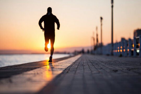 Blurred silhouette of a man jogging along a seaside promenade at sunrise