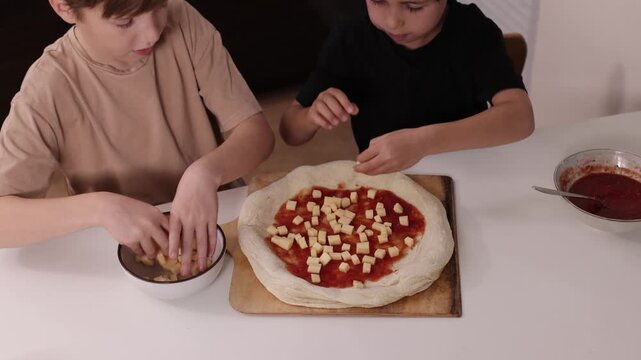 Children preparing pizza at home and spreading white sauce on dough, concept of family cooking, learning and creativity.