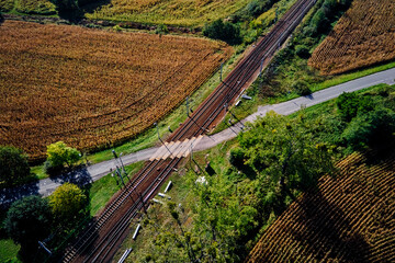 Aerial view of railway tracks crossing rural road surrounded by fields and trees. Concept of...