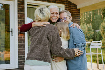 Senior Caucasian woman embracing middle aged man, woman, and young girl outdoors, all smiling and...