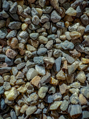 An extremely close-up and highly textured view of small, wet-looking river pebbles in natural shades of blue, green, orange, and grey under dramatic lighting.