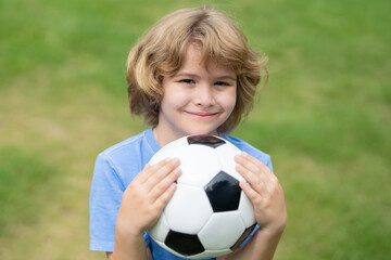 A happy kid holds a soccer ball. Kid football player portrait. Child shows football ball. Little soccer player enjoys sports outdoors. Boy playing football. The boy dreams of football success.