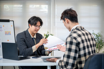 Glasses asian businessman reading documents talking to employee at working table in company's office
