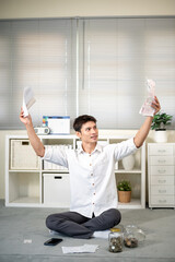 Frustrated asian man office worker holding and looking at bills as sitting on the living room floor.
