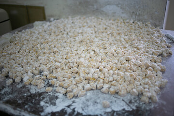 A large tray filled with tiny, flour-dusted dough balls ready for baking in a commercial bakery. Fresh, artisanal treats prepared for cookies or pastries in a busy production setting.
