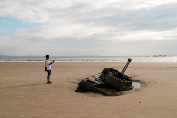 A South Asian man on the sandy beach talking photos of the remains of an old destroyed war tank in Kinmen.