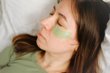 Beautiful 40s woman with cosmetic patches under the eyes. Female takes care of her face skin in the...