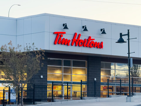 Calgary, Alberta, Canada. Oct 29, 2025. Tim Hortons storefront features iconic red logo on contemporary building with black railing patio, glowing interior lights at twilight hour