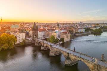 Morning sunlight gently illuminates Prague Castle in the background, while people stroll across Charles Bridge over the Vltava River, creating a serene early day scene in Prague.