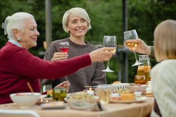 Family members sitting outdoors raising wine and juice glasses together, smiling and enjoying meal at table