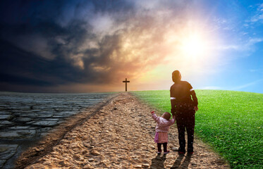 Silhouette of a mother and his daughter standing on a path leading to the cross