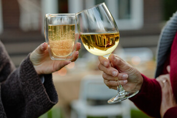 Caucasian middle aged woman and Caucasian senior woman clinking glasses outdoors, holding wine and sparkling beverage, celebrating together in garden setting, hands visible only