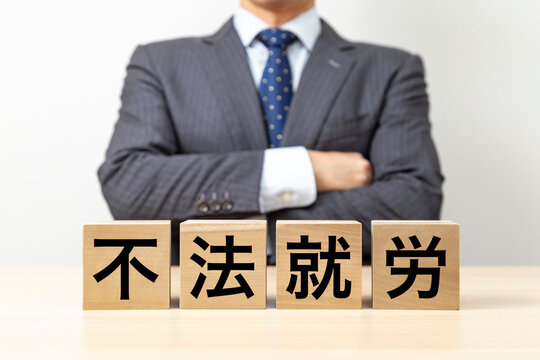 「不法就労」と書かれたブロックと腕組みをするビジネスマン