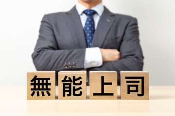 Obraz premium 「無能上司」と書かれたブロックと腕組みをするビジネスマン