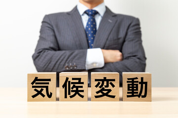 「気候変動」と書かれたブロックと腕組みをするビジネスマン