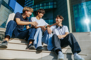 Three teenage boys chatting and smiling while sitting on outdoor stairs