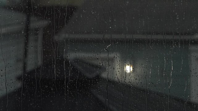 Dreamy, cinematic view of rainfall on a windowpane looking outward toward a glowing building in the distance.