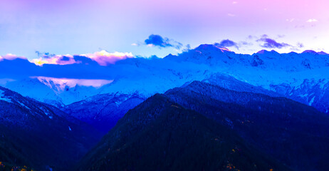 Landscape view of sunset illuminates the rugged, snow-capped mountain peaks under a twilight sky ...