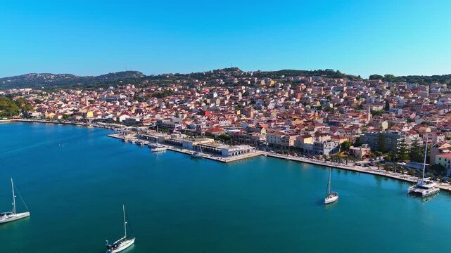 Cinematic aerial footage of Argostoli, the charming capital of Kefalonia Island in Greece. The clip captures the picturesque harbor, colorful waterfront houses, and boats gliding over the Ionian Sea.