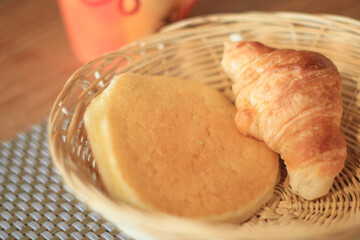 Warm and cozy breakfast meal featuring golden croissant and fluffy pancake in wicker basket. An appetizing and comforting morning food selection served with hot beverage