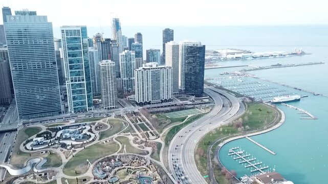 Aerial drone video slowly panning the left showing highway traffic next to a lake and marina while showing the skyline buildings in downtown Chicago, Illinois.