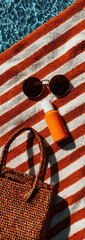 Close up photography of a hat, sunglasses and other beach accessories on a towel on the sand of a beautiful beach.