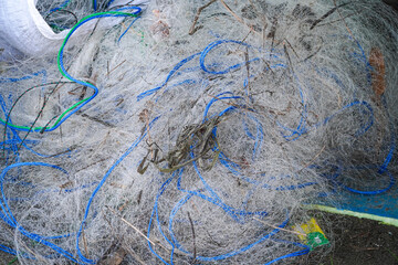 A detailed close-up showcasing a tangled mass of thin, white netting interspersed with vibrant blue and green ropes. Sticks and natural debris are embedded within the netting.