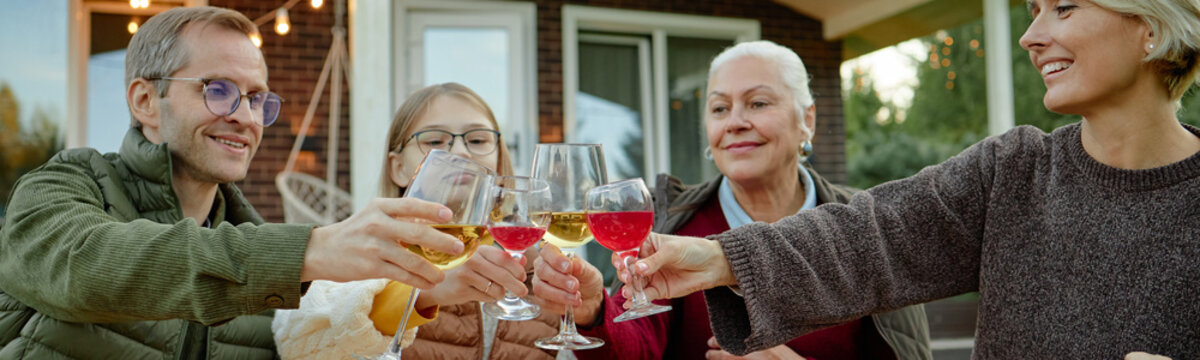 Header of Caucasian man, Caucasian teenage girl, Caucasian senior woman, Caucasian middle aged woman clinking glasses outdoors, smiling and celebrating together in front of house
