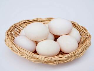 Severil large duck eggs are placed in a wicker basket on a white background.