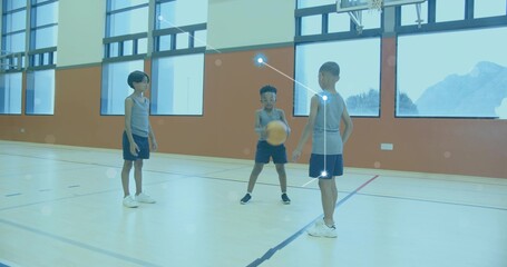 Dribbling basketball, three boys wearing grey jerseys and navy shorts on gym court near hoop
