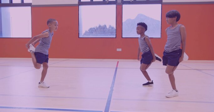 Fototapeta Stretching 3 boys balancing on one foot holding ankle in school gym wearing grey sleeveless shirts